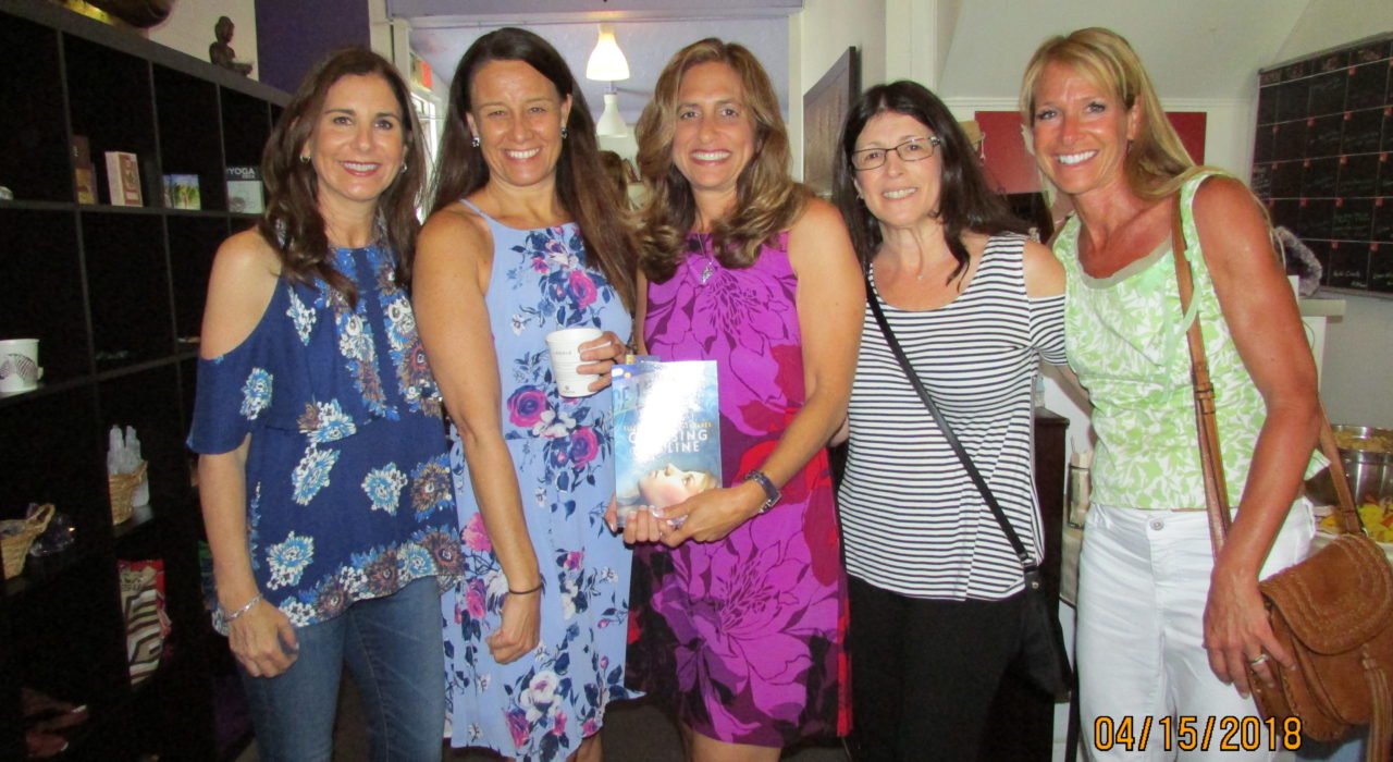 Five women, the one in the middle holding a book